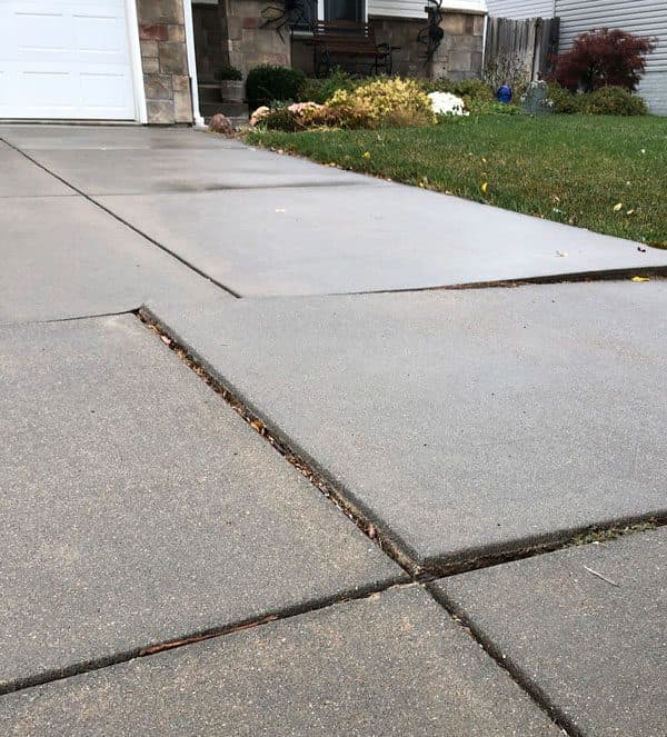 Concrete driveway slabs beside a garage, with one slab settled lower than its neighbor and an uneven joint between them.