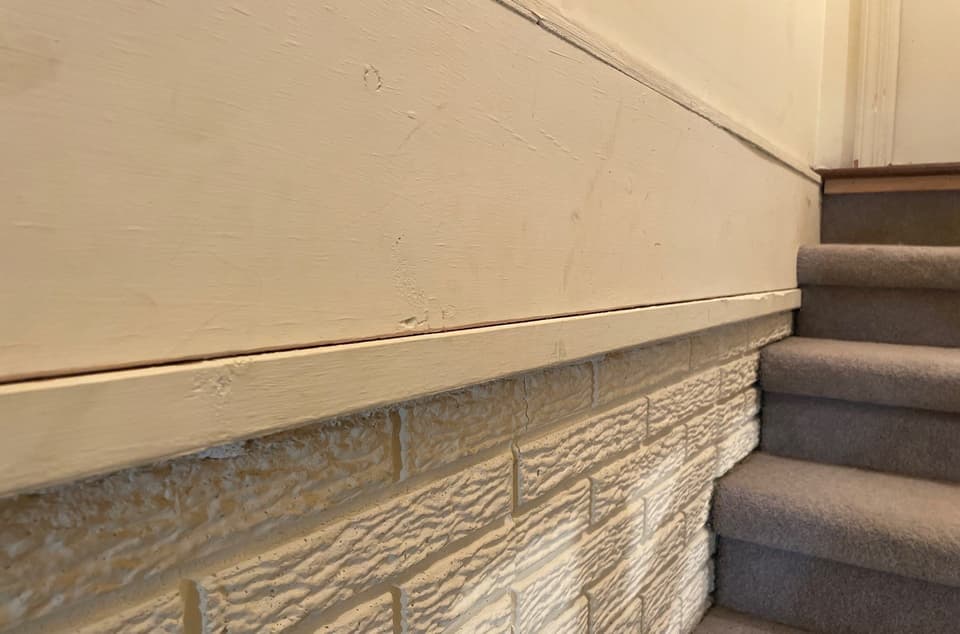 Completed foundation repair work showing wall anchors installed on a brick foundation wall with smooth finished upper wall and carpeted stairs visible.