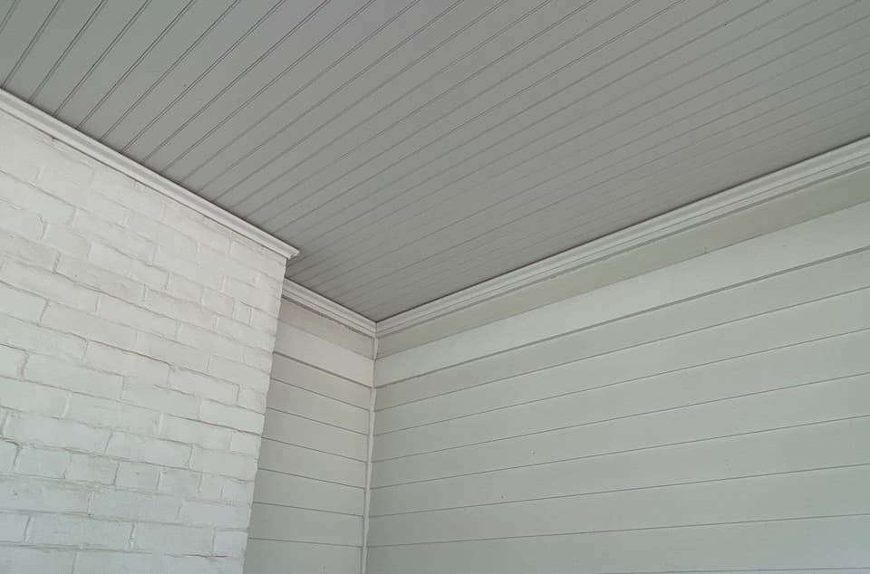 A finished crawlspace or basement area with white painted brick walls, horizontal wood or vinyl paneling on the right wall, and a gray vinyl plank ceiling, showing completion of encapsulation work.