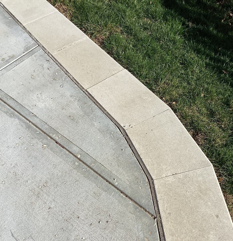 Completed concrete flatwork installation along a property edge with new concrete pavers adjoining existing concrete and grass landscaping.