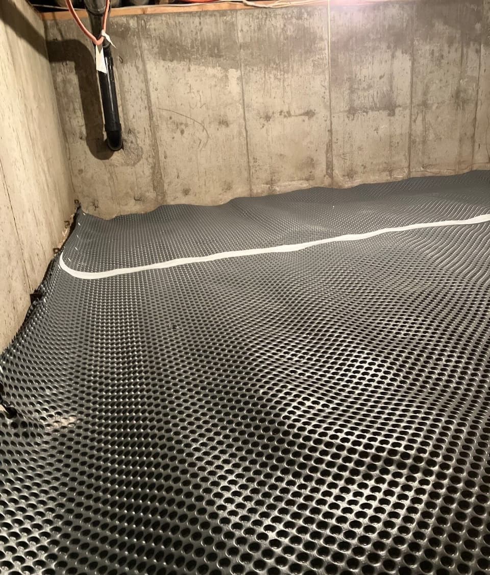 A completed crawlspace with installed dimple membrane flooring, drainage channel, and encapsulation system in a basement with concrete walls.