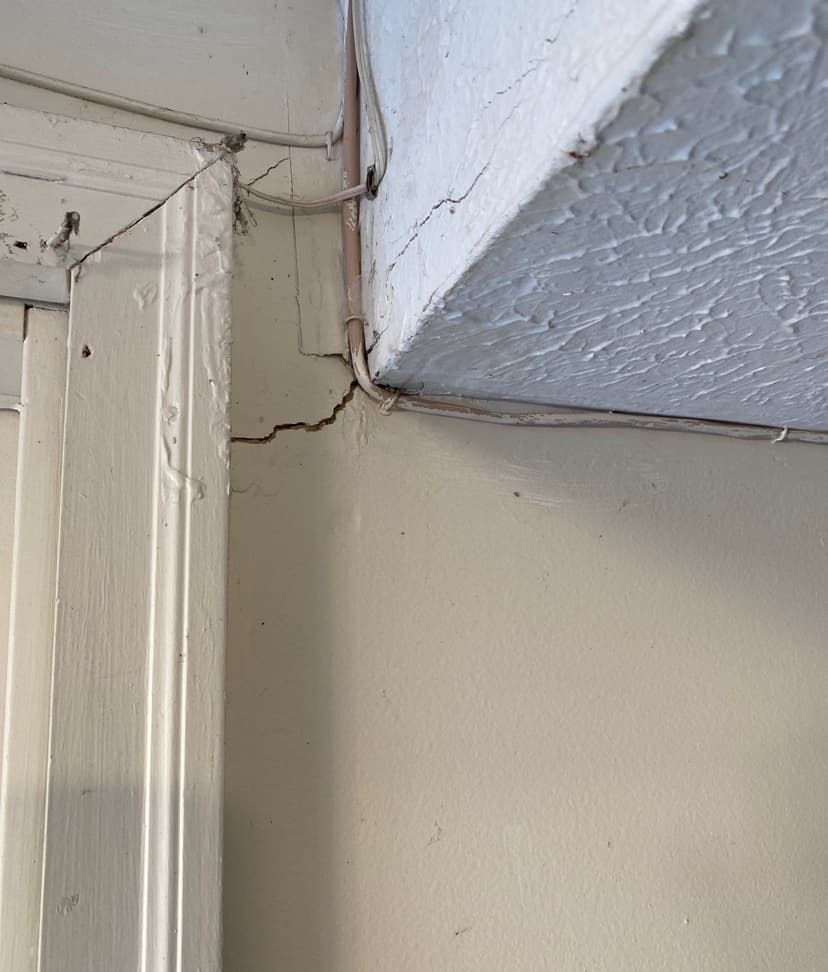 Epp Foundation Repair inspecting a diagonal drywall crack in a ceiling corner, indicating structural stress.