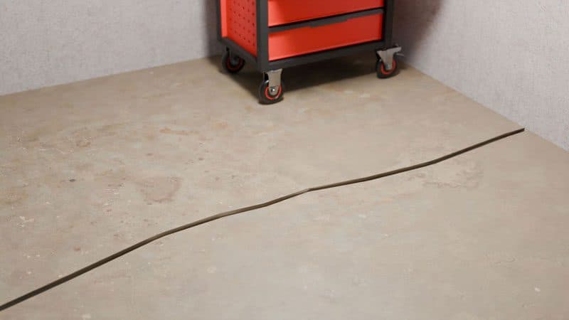 Epp Foundation Repair inspecting a long crack in a concrete garage floor near a tool chest.