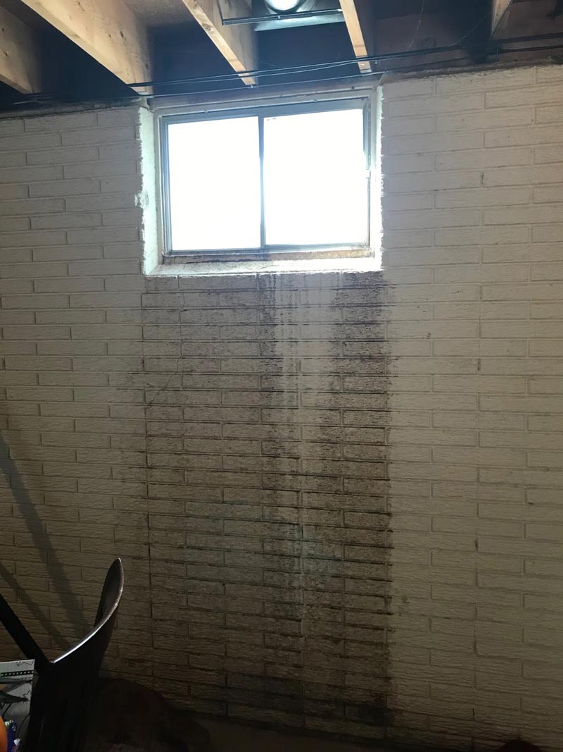Painted masonry basement wall with dark water stains running down below a basement window