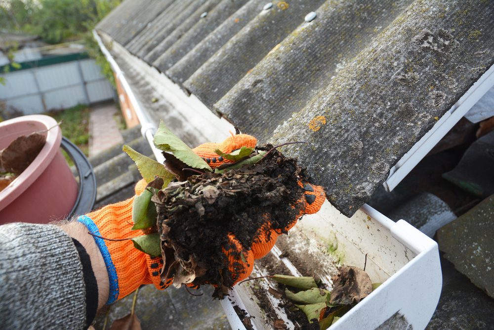 Gloved hand scooping debris out of a clogged gutter