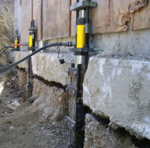 Foundation underpinning is a repair process that involves excavation down to the footing and the addition of push or helical piers to stabilize and support the foundation. Once the piers are in place, the foundation is raised using a synchronized hydraulic lifting system.